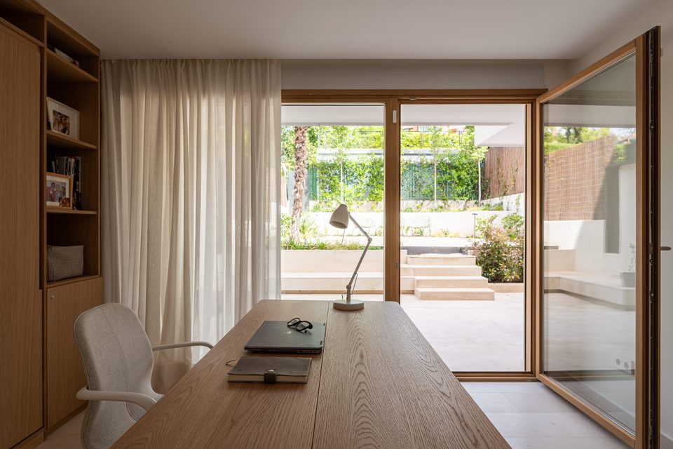 Despacho con mesa de roble y un cerramiento de madera y vidrio que da a una terraza ajardinada