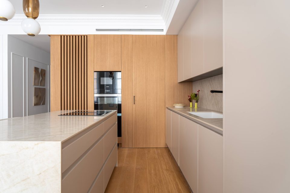 Cocina con armario alto de listones y puertas de roble, isla de piedra y muebles lisos