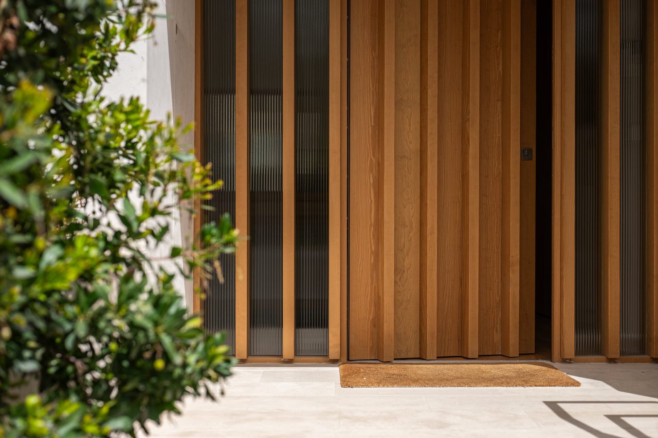 Puerta de listones de madera con paneles de vidrio acanalado y vegetación en primer plano